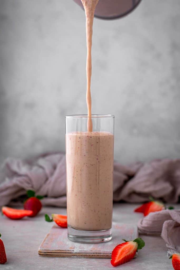 keto strawberry smoothie Pouring a glass of strawberry smoothie into a clear tall glass